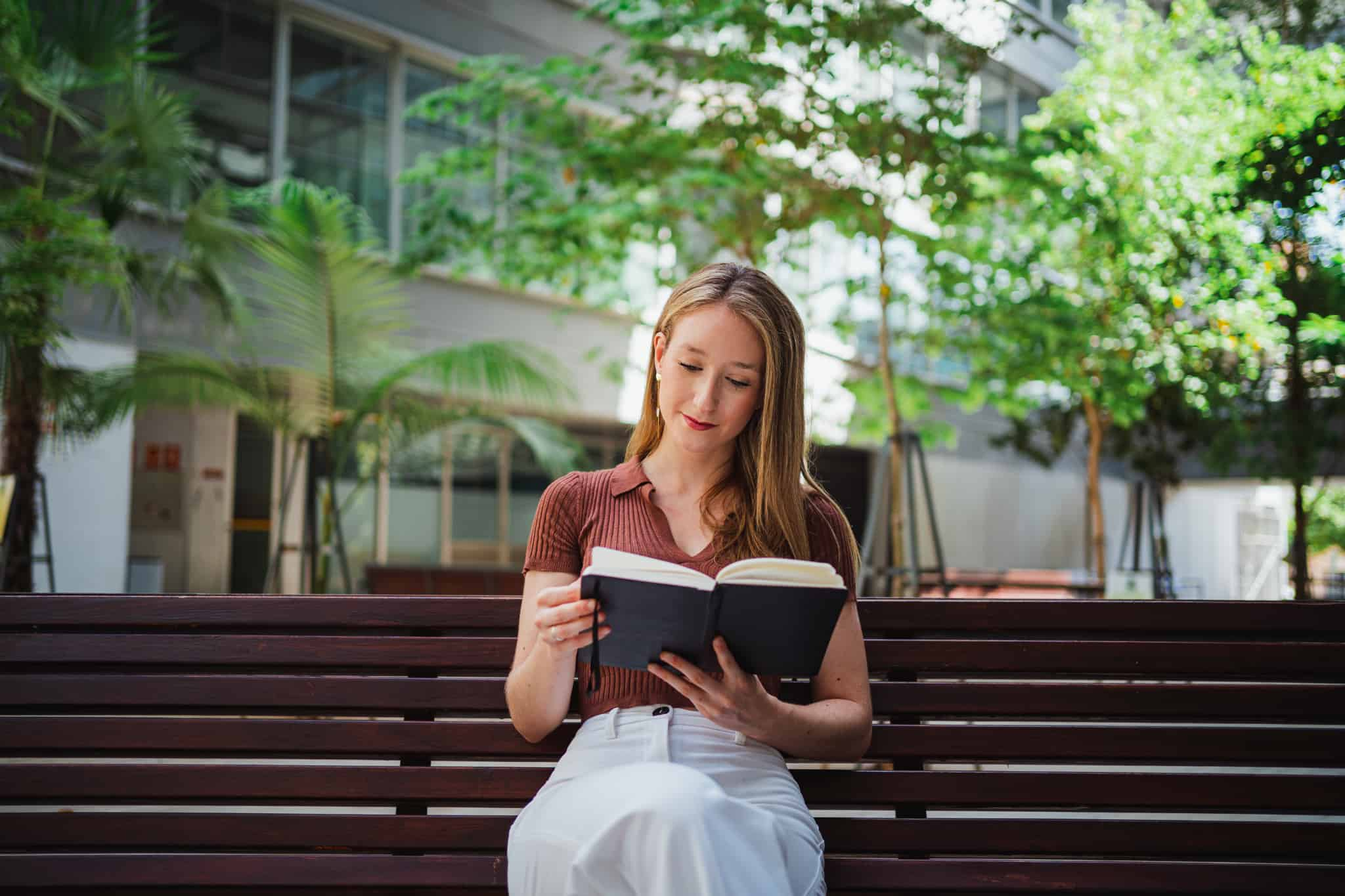 外のベンチに座って本を読む女性