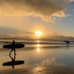 朝日が昇る海辺でサーフィンをする人たち